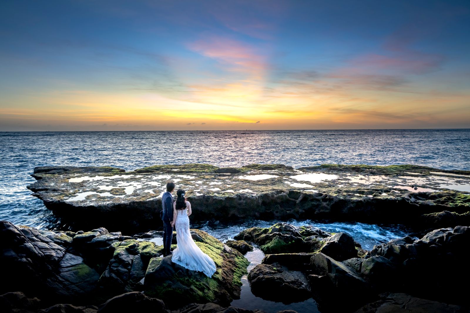 Couple standing together on a rocky shore during golden hour